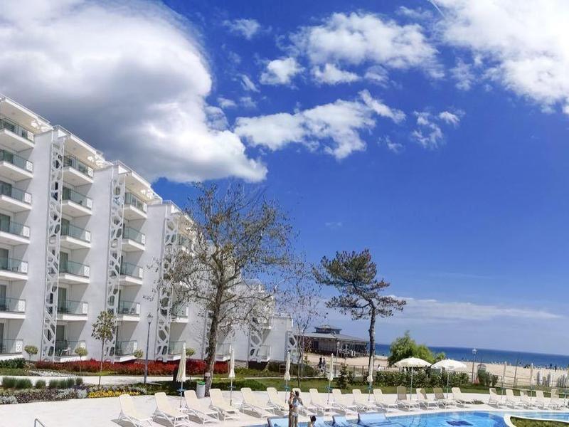 Moderní hotelový komplex s bazénem, palmami a výhledem na útesy pod modrou oblohou.