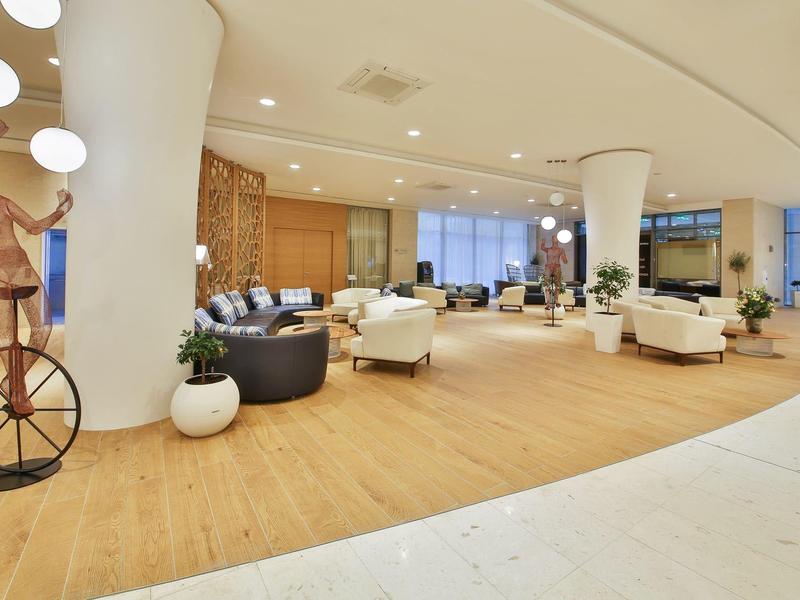 Světle hotelové lobby s moderním nábytkem, dřevěnou podlahou a sochou na jednokolce.
