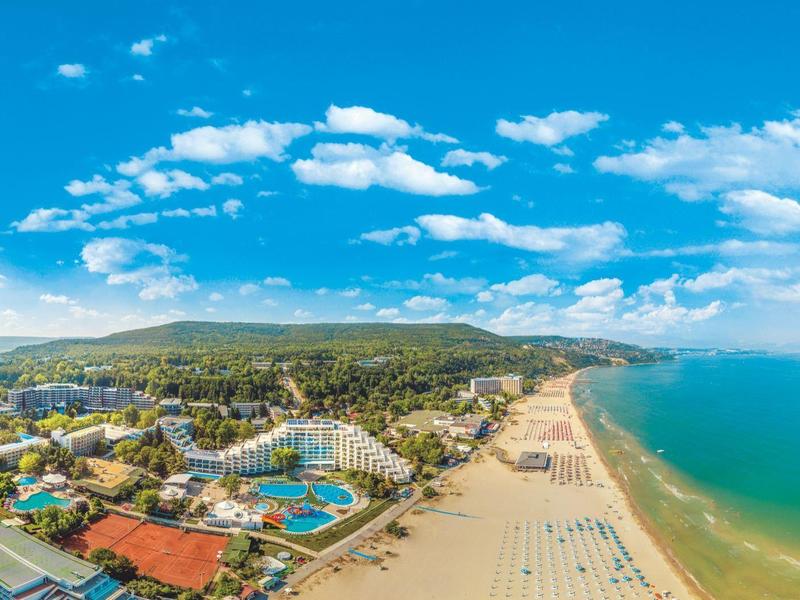 Panorama plážového resortu s bazény, lehátky a jasně modrou oblohou.