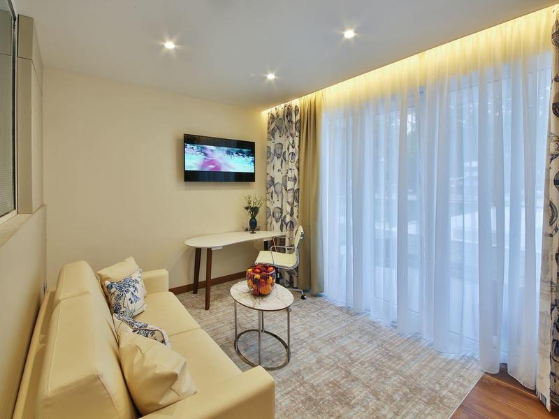 Moderní obývací pokoj s pohovkou, závěsy a TV, světlé osvětlení.