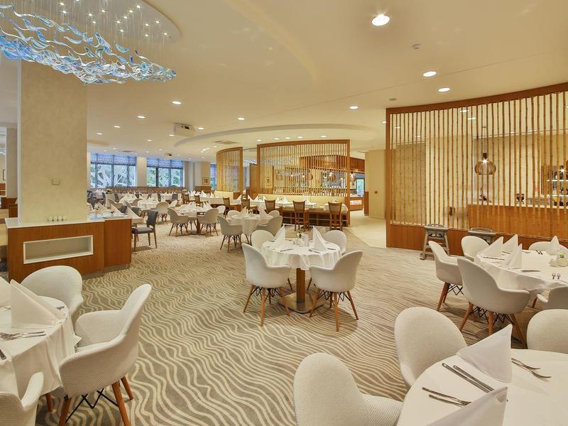 Elegantní hotelová restaurace s bílými ubrusy a moderním posezením v světlém prostředí.