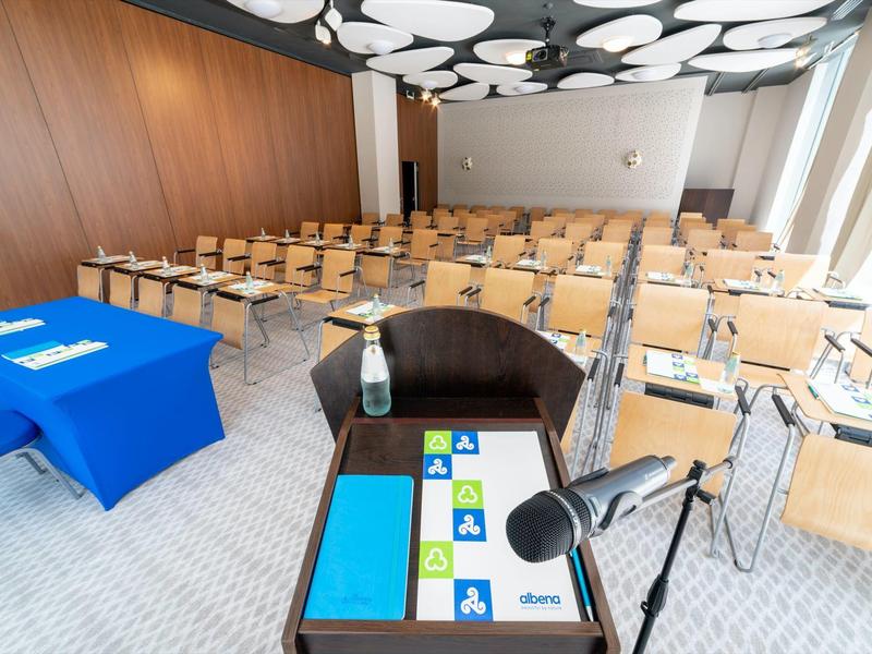 Moderní konferenční místnost s dřevěnými židlemi a řečnickým pultem s mikrofonem.