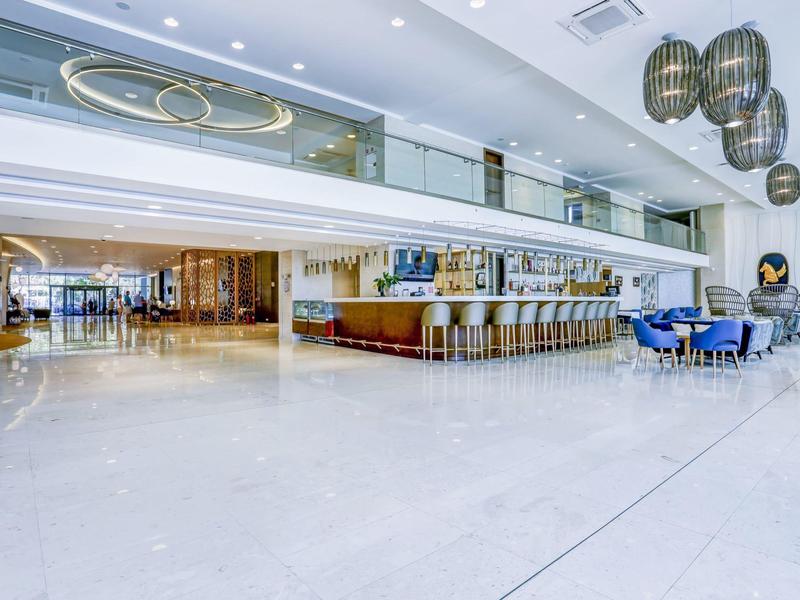 Velká hotelová hala s úsporným nábytkem, barem a moderním osvětlením.