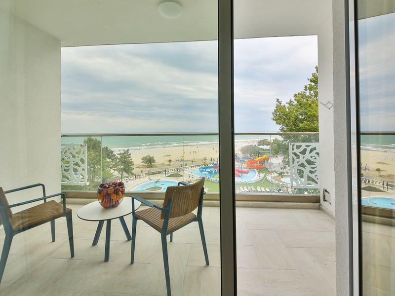 Balkon s stolem a židlemi s výhledem na pláž a moře za zatažené oblohy