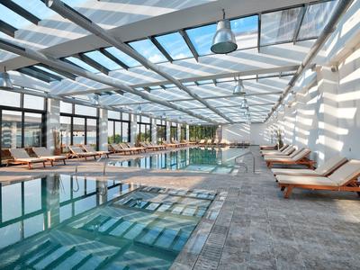 Área moderna de piscina interior con tumbonas y techo de cristal en ambiente luminoso.