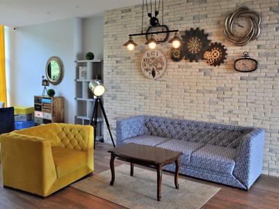 Sala moderna de hotel con sillón amarillo, sofá azul, suelo de madera y decoraciones de pared metálicas.