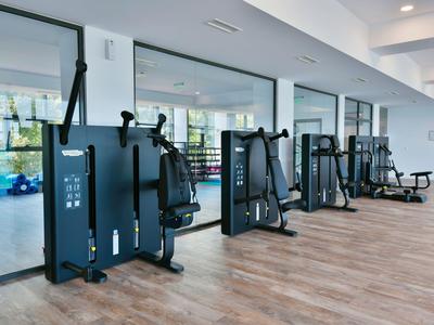 Moderne hotelgym met verschillende krachttrainingsapparaten en houten vloer.