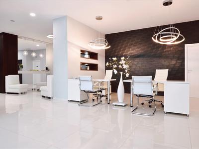 Área moderna de salón de hotel con sillones blancos, mesas y iluminación elegante en el techo.