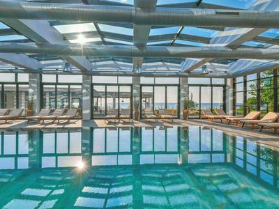 Piscina interior con tumbonas y grandes ventanas que dejan entrar la luz del día.