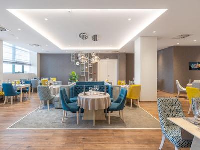 Área de restaurante moderno del hotel con sillas coloridas, mesas e iluminación elegante en espacio luminoso.