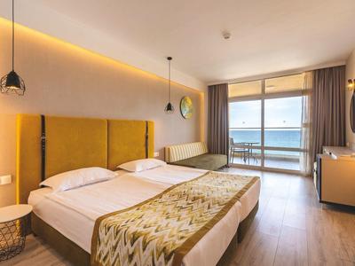 Habitación de hotel iluminada con cama doble y vista al mar a través de grandes ventanales.