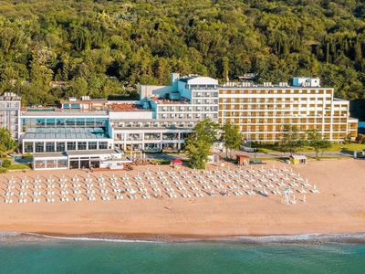 Gran hotel junto a una colina boscosa con playa y filas de tumbonas junto al mar.