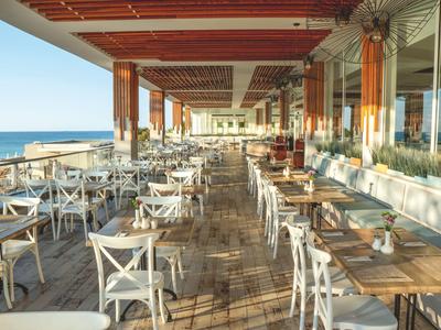 Restaurante abierto con sillas blancas y vista al mar al atardecer.