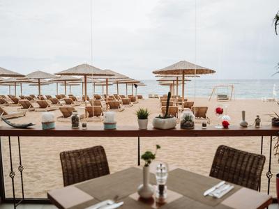 Tafel met bestek op restaurantterras met uitzicht op zandstrand met zonneschermen en zee.