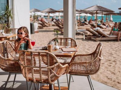 Mujer sentada en una mesa con sillas de mimbre en hotel de playa con sombrillas al fondo.