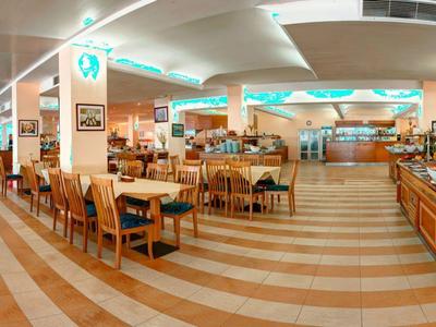 Amplio comedor luminoso con sillas de madera y área de buffet en un hotel.