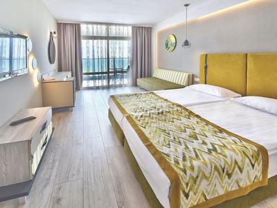 Modernes Hotelzimmer mit Doppelbett, Fernseher und großer Fensterfront mit Gardinen.