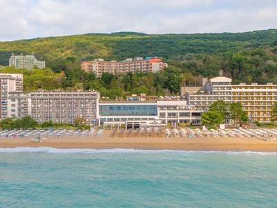 Hotel de playa con varios edificios frente a colina boscosa y mar tranquilo en primer plano
