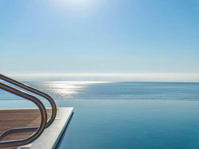 Ein klarer Himmel spiegelt sich in einem ruhigen Infinity-Pool am Meer wider.