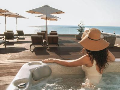 Frau entspannt im Whirlpool mit Blick auf sonnige Poolliegen und Meer.