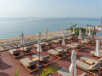 Blick auf eine Terrasse mit Liegestühlen und geschlossenen Sonnenschirmen am Meer.