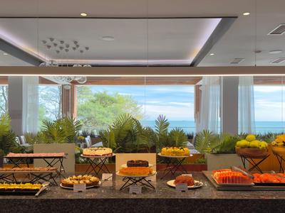 Moderner Frühstücksraum mit Ausblick auf Garten und Meer, Buffet mit Obst und Backwaren.