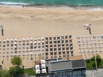 Luftaufnahme eines Strandes mit Reihen von Sonnenschirmen und einem angrenzenden Hotelgebäude.