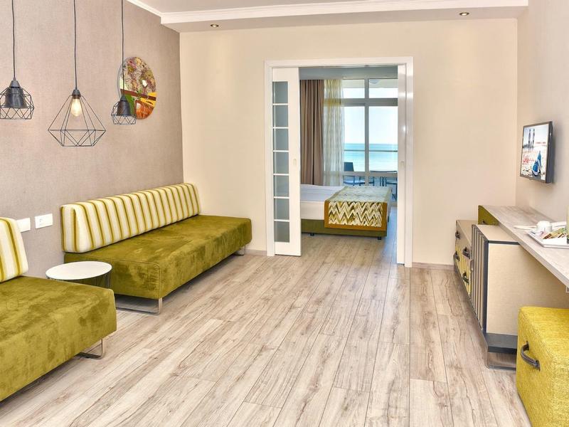 Una habitación de hotel moderna con sofás verde amarillentos y suelo de madera clara.