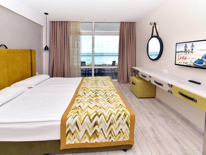Habitación de hotel moderna con cama grande, detalles amarillos, escritorio y vista al mar.
