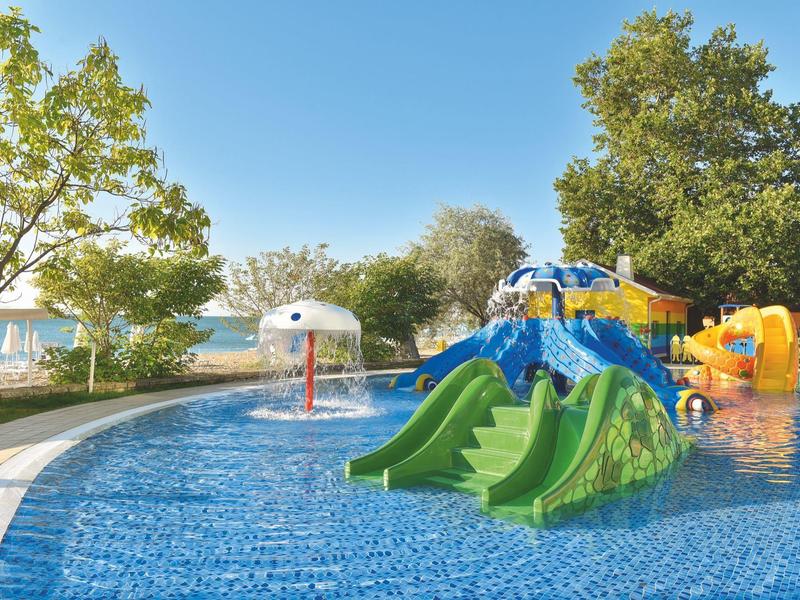 Piscina recreativa con toboganes acuáticos coloridos y juegos de agua en un jardín bajo cielo azul.