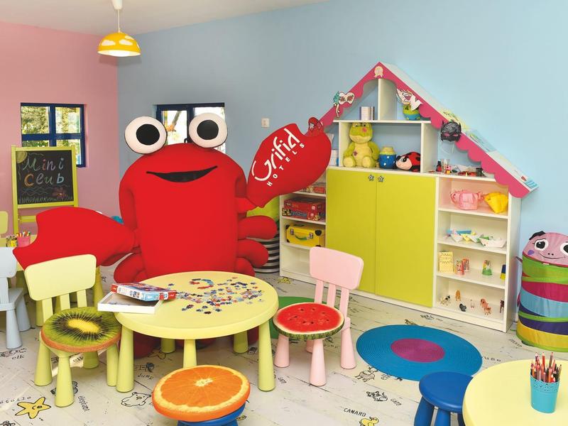 Sala de juegos infantil colorida con mesas, sillas y figura de cangrejo en la pared.
