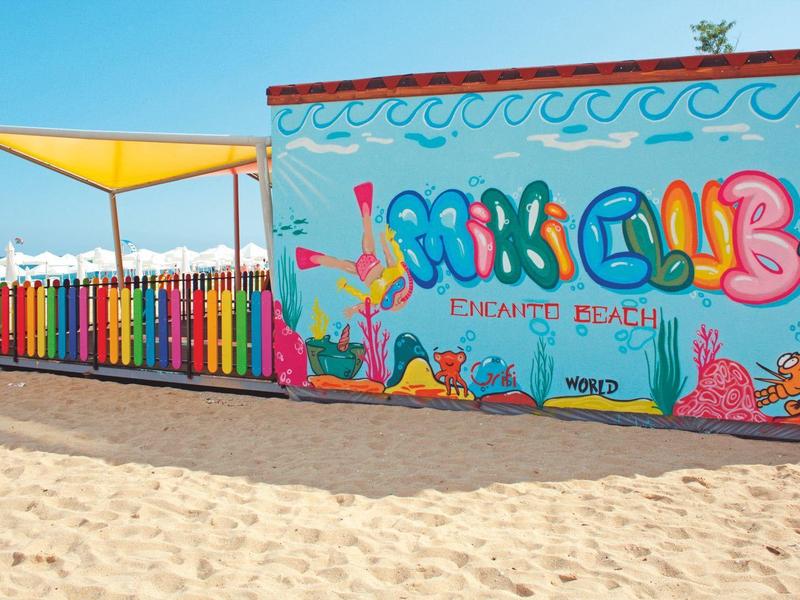 Bar de playa pintada de colores con toldo, arena y cielo azul de fondo.