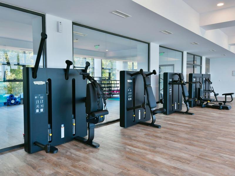 Equipos de gimnasio modernos en una sala de fitness brillante de hotel con suelo de madera y espejos grandes.
