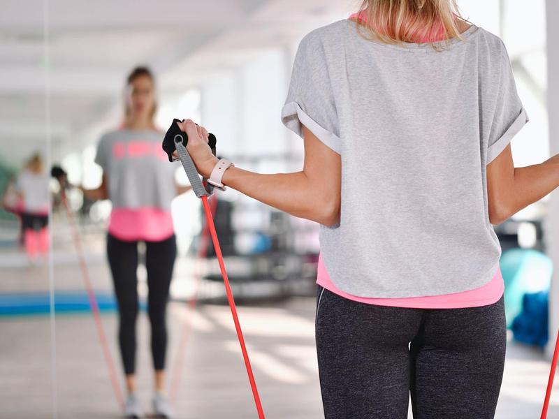 Mujer entrena con banda de resistencia frente a un gran espejo en la sala de fitness del hotel.