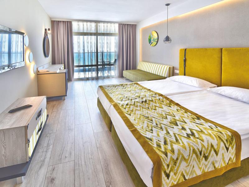 Habitación de hotel moderna con dos camas, cabecero amarillo y gran ventana con cortinas.