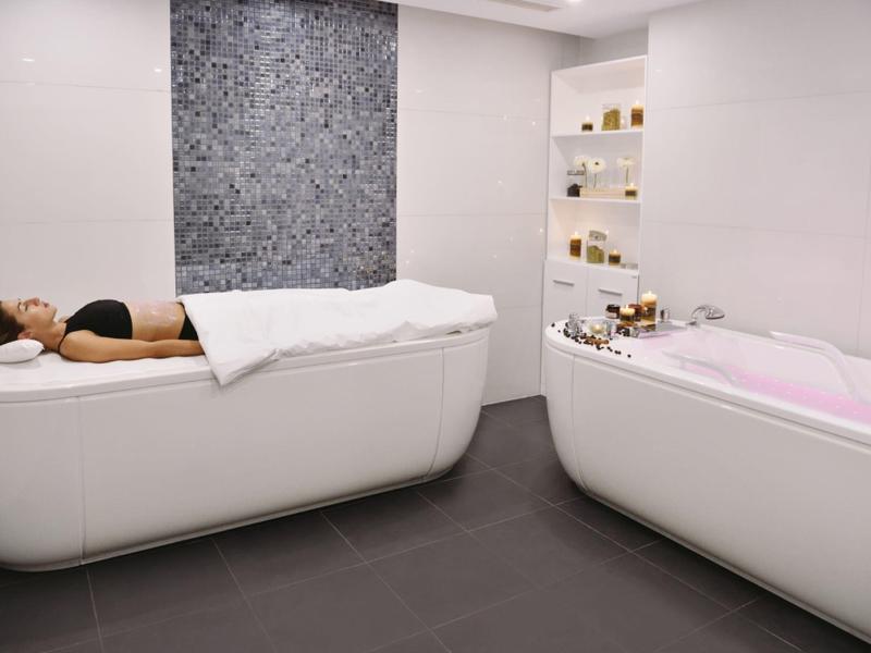 Instalación moderna de spa con banco de relajación y bañera en habitación blanca.