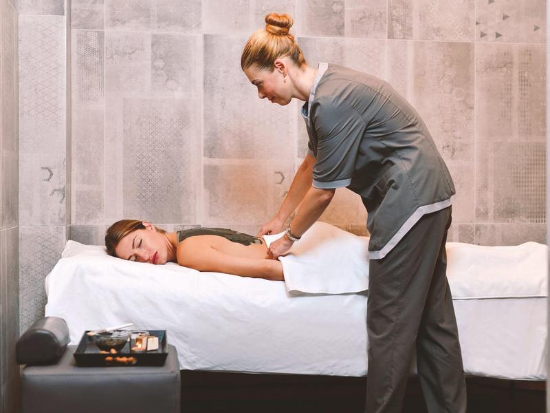 Una persona recibe un masaje de espalda en una sala de bienestar moderna y tranquila con paredes grises.