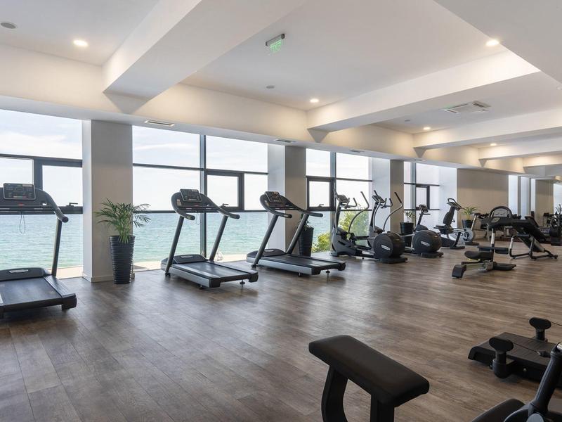 Gimnasio moderno con cintas de correr, pesas, grandes ventanas y suelo de madera.