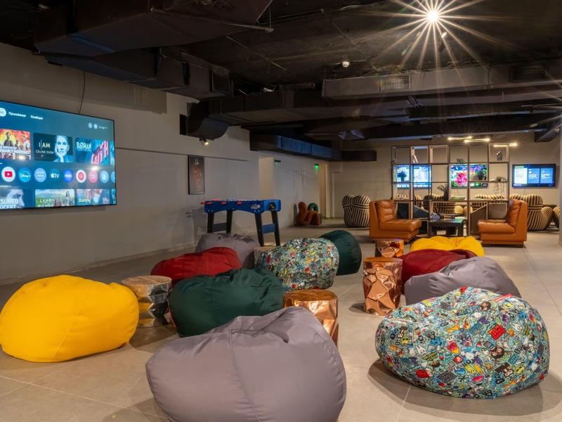 Área de descanso acogedora con puffs coloridos, televisión y sofás.
