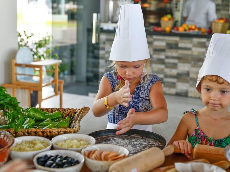 Dos niños con gorros de chef preparan masa en una cocina llena de ingredientes.