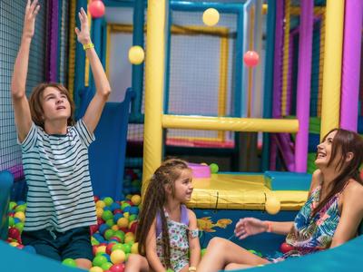 Tres niñas juegan felices en una piscina de bolas coloridas en un parque infantil interior.