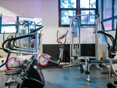 Innenansicht eines Fitnessraums mit verschiedenen Trainingsgeräten und großen Fenstern.