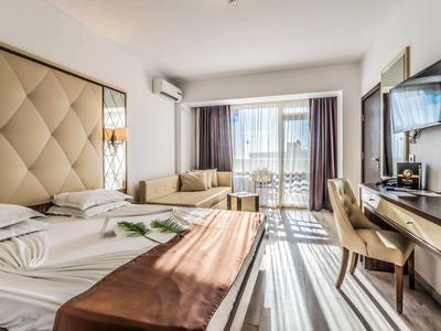 Habitación de hotel moderna con cama grande, sofá, escritorio y balcón con vista al mar.