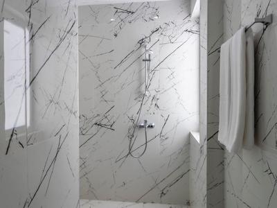 Ducha moderna con azulejos de mármol blanco y negro y toallas blancas colgadas en la pared.