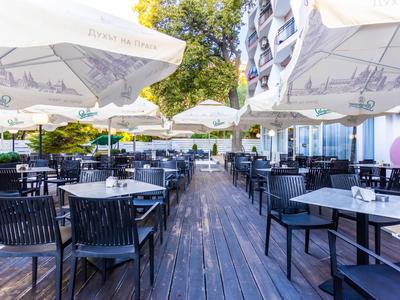 Terrasse im Freien mit schwarzen Stühlen, Tischen und weißen Sonnenschirmen bei Tageslicht.