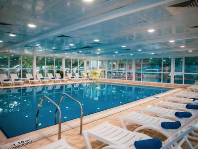 Piscina interior de hotel con tumbonas blancas y toallas azules.
