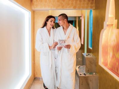 Pareja con albornoces relajándose y riendo en un pasillo de hotel.