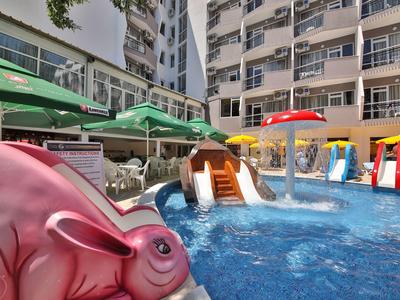 Zona de juegos infantiles con toboganes y juegos de agua junto a la piscina del hotel y sombrillas.