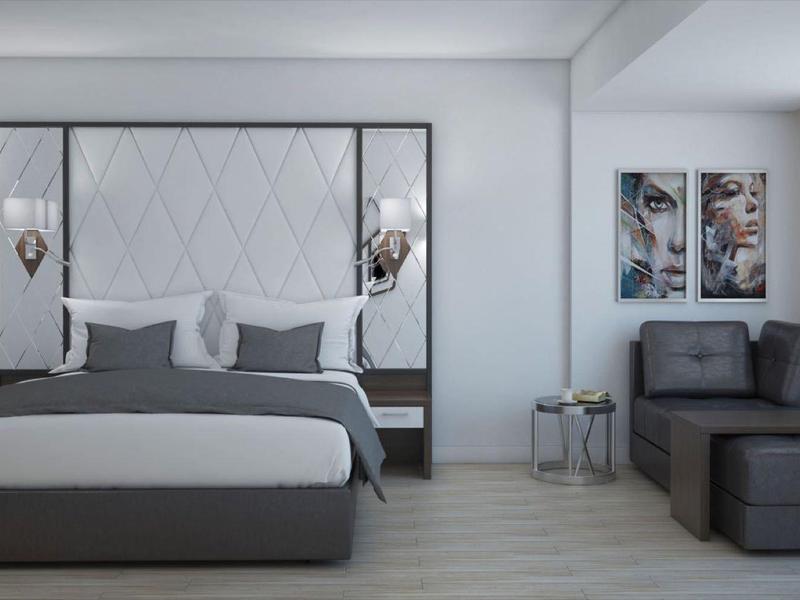 Habitación de hotel moderna con cama grande, zona de estar y esquema de colores neutro.