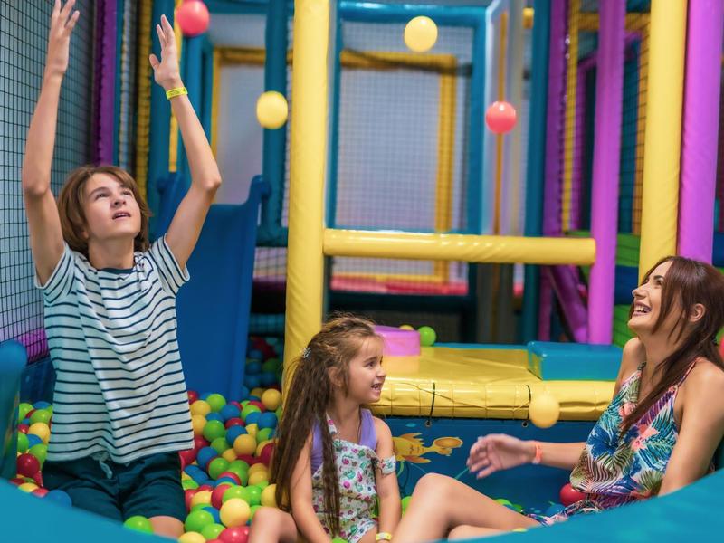 Tres niñas juegan felices en una piscina de bolas coloridas en un parque infantil interior.